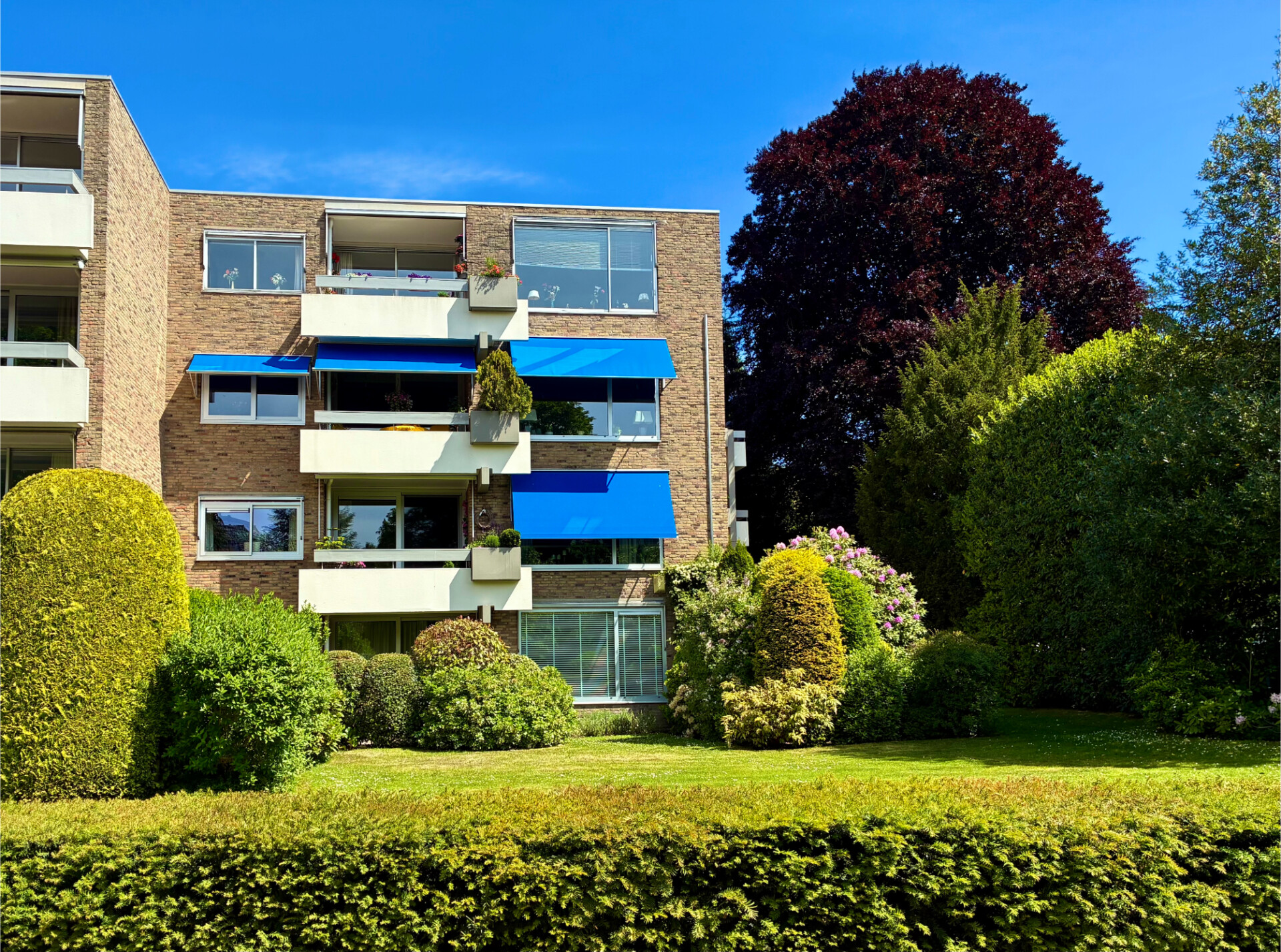 Blauwe uitvalschermen als zonwering boven de balkons van een appartementencomplex.