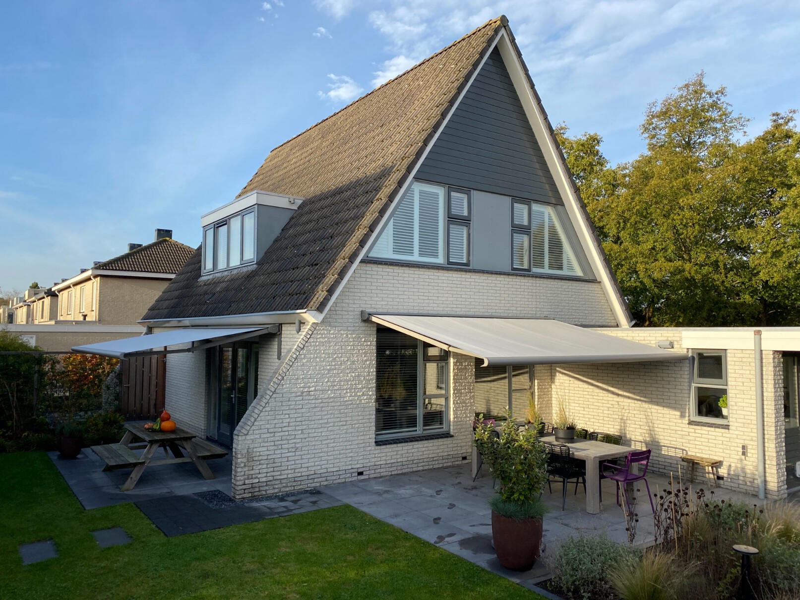 Balero knikarmschermen met crème doek aan twee kanten van een woning met puntdak.