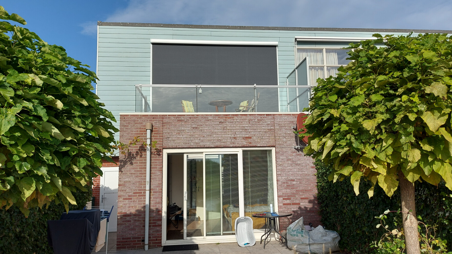Antracietkleurige screen als elektrische zonwering bij een balkon aan een woonhuis.
