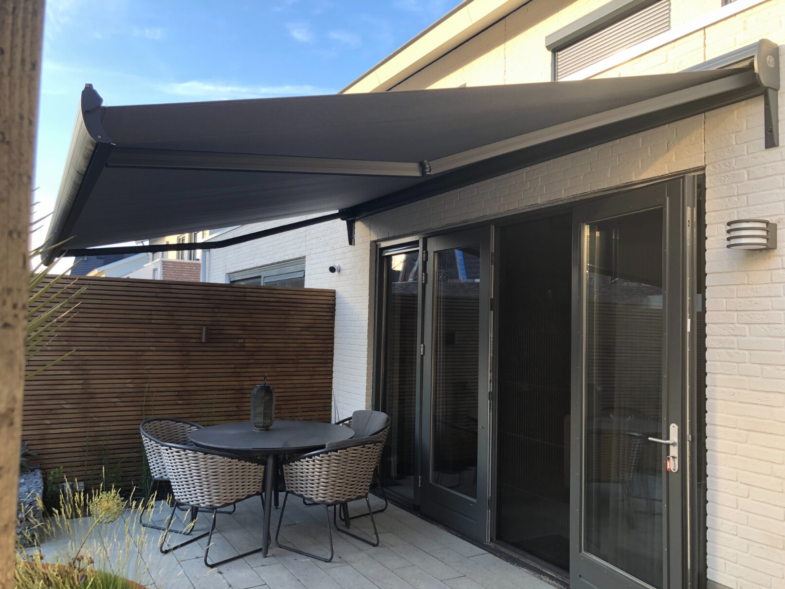 Knikarmscherm Ibiza Plus met antraciet doek en frame als terrasoverkapping tegen een witte gevel.
