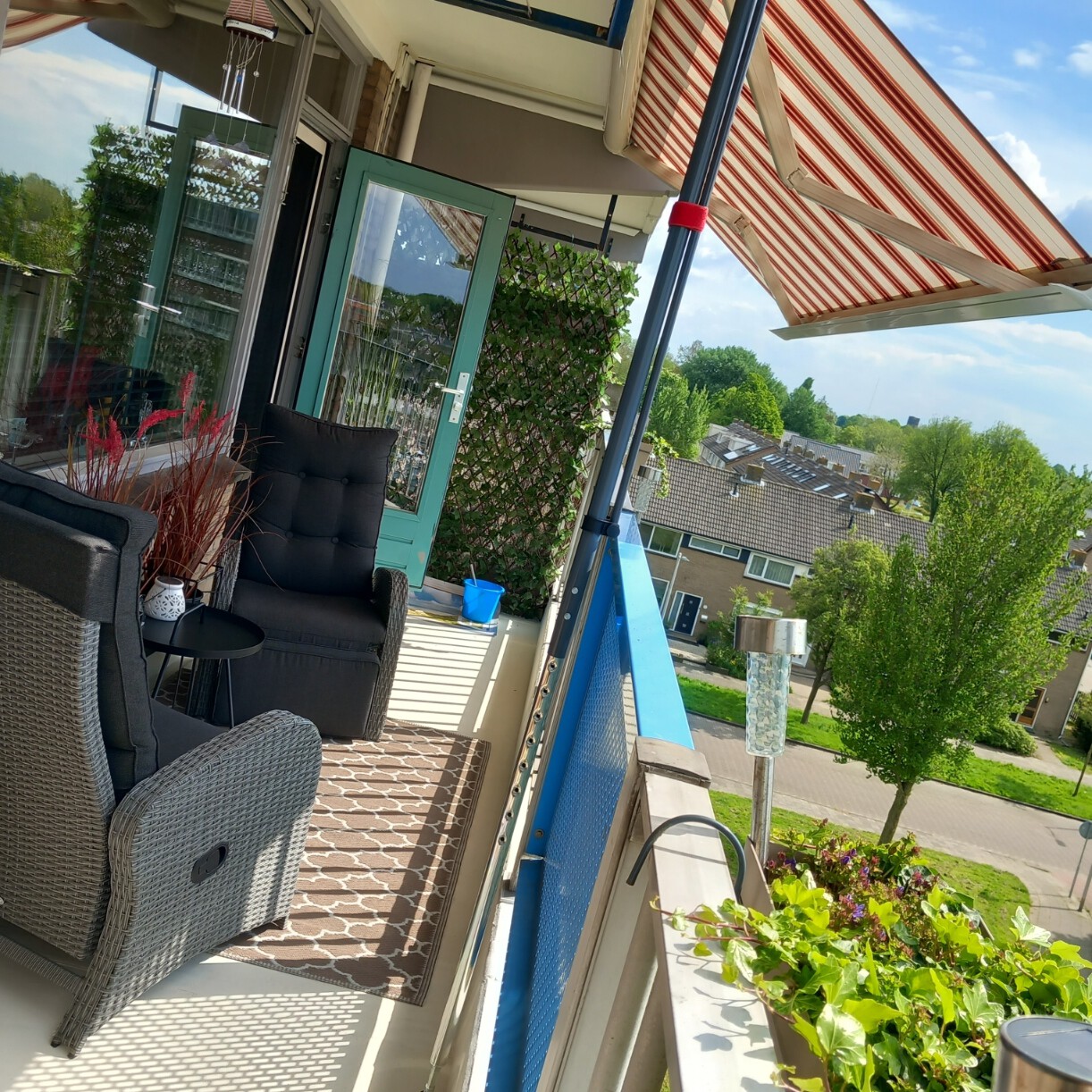 Zonnescherm met rood-wit gestreept doek en knikarmsysteem op een balkon van een appartement.