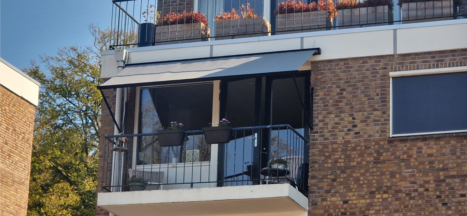 Horizontaal zonnescherm voor het balkon van een appartement met een grijs doek en een uitvalsysteem.