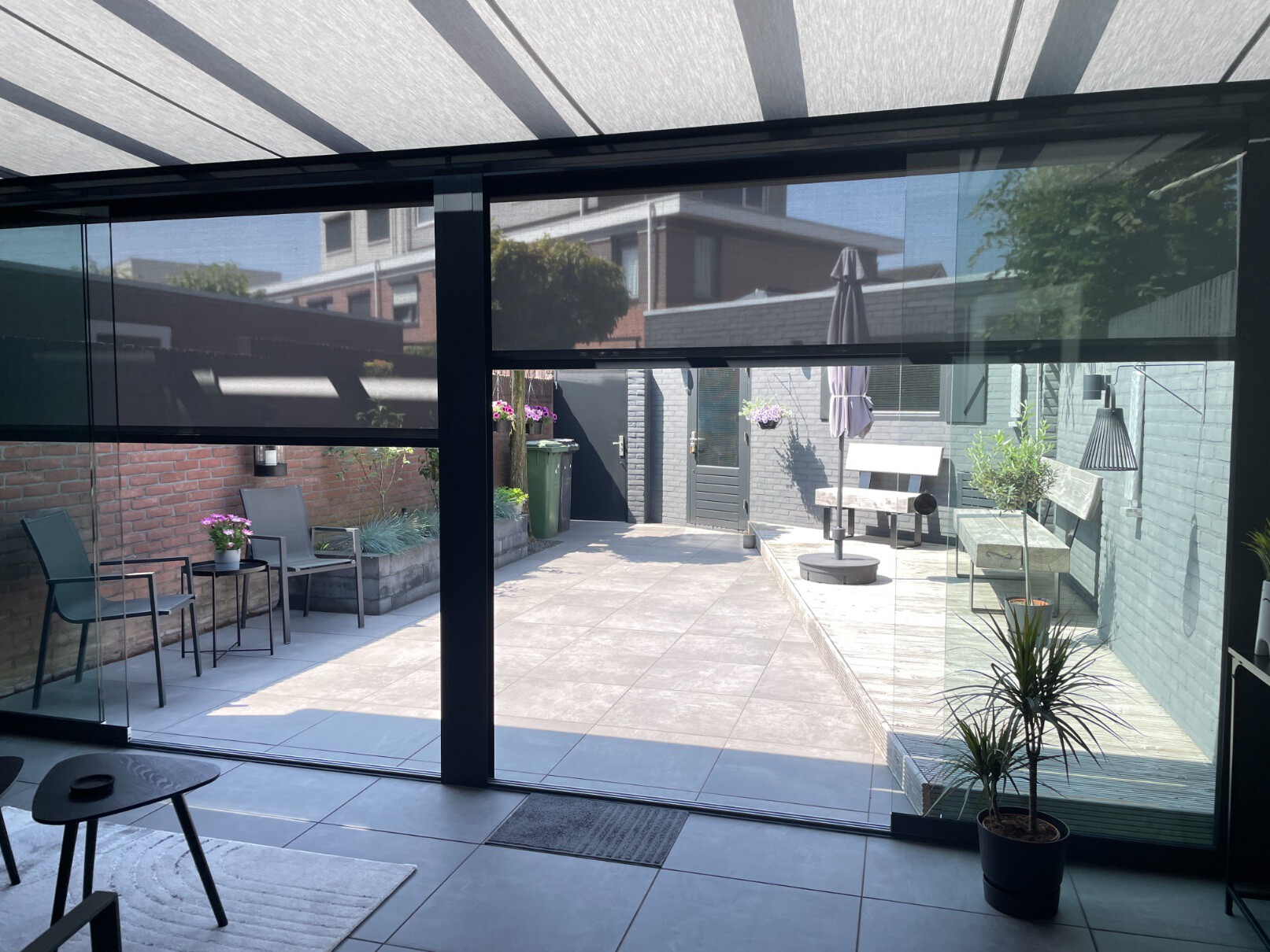 Antracietkleurige screens voor een overkapping met zijpanelen in een tuin met lichte tegels.