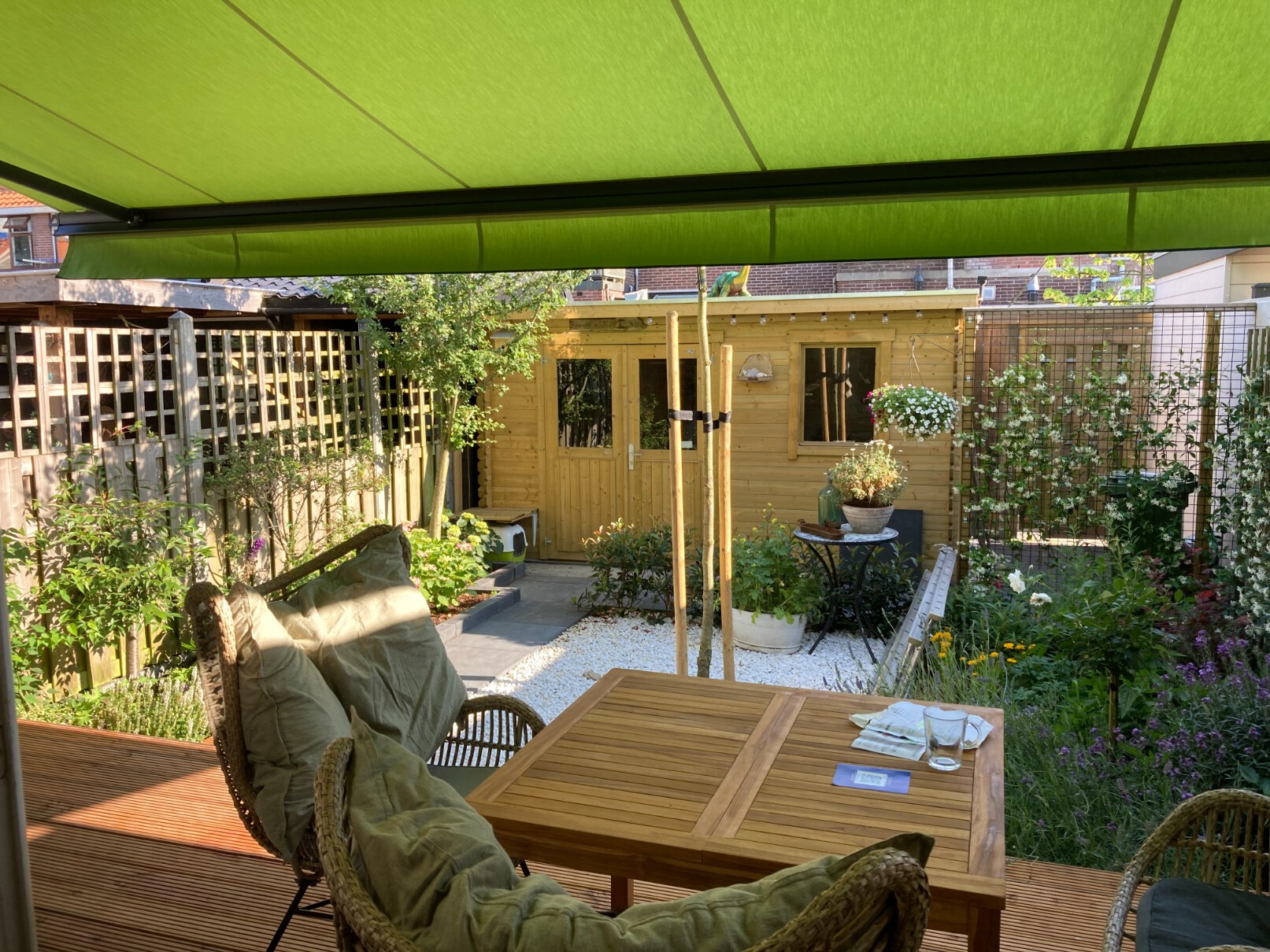 Zonnescherm met frisgroen doek en knikarmsysteem boven een houten terras en uitzicht op de tuin.