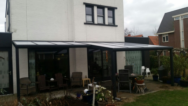 Fiësta overkapping met dak dat verspringt in breedte tegen een witte gevel aangebouwd.